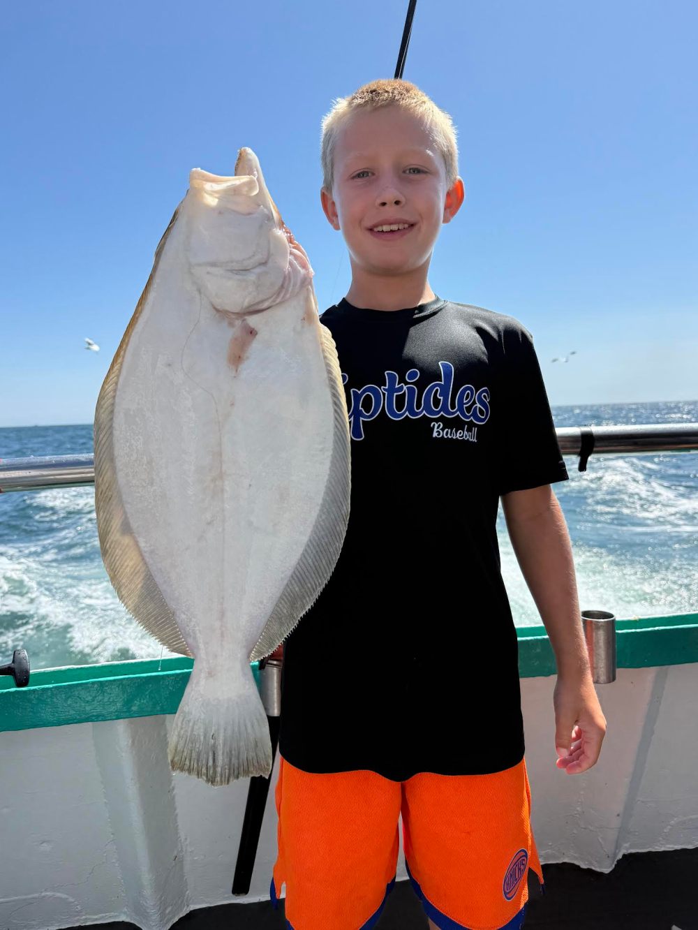 Child holding a large fish on a boat with the ocean in the background.