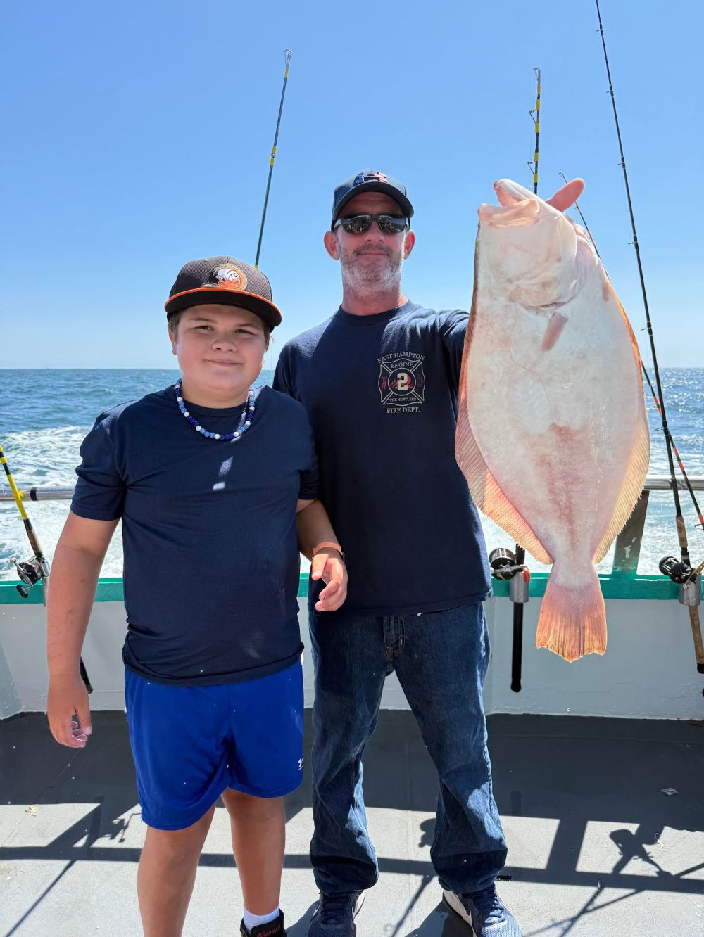 Two people on a boat holding a large fish with fishing rods in the background.