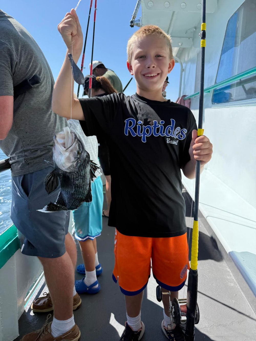 Child on a boat holding a fish and a fishing rod, smiling.