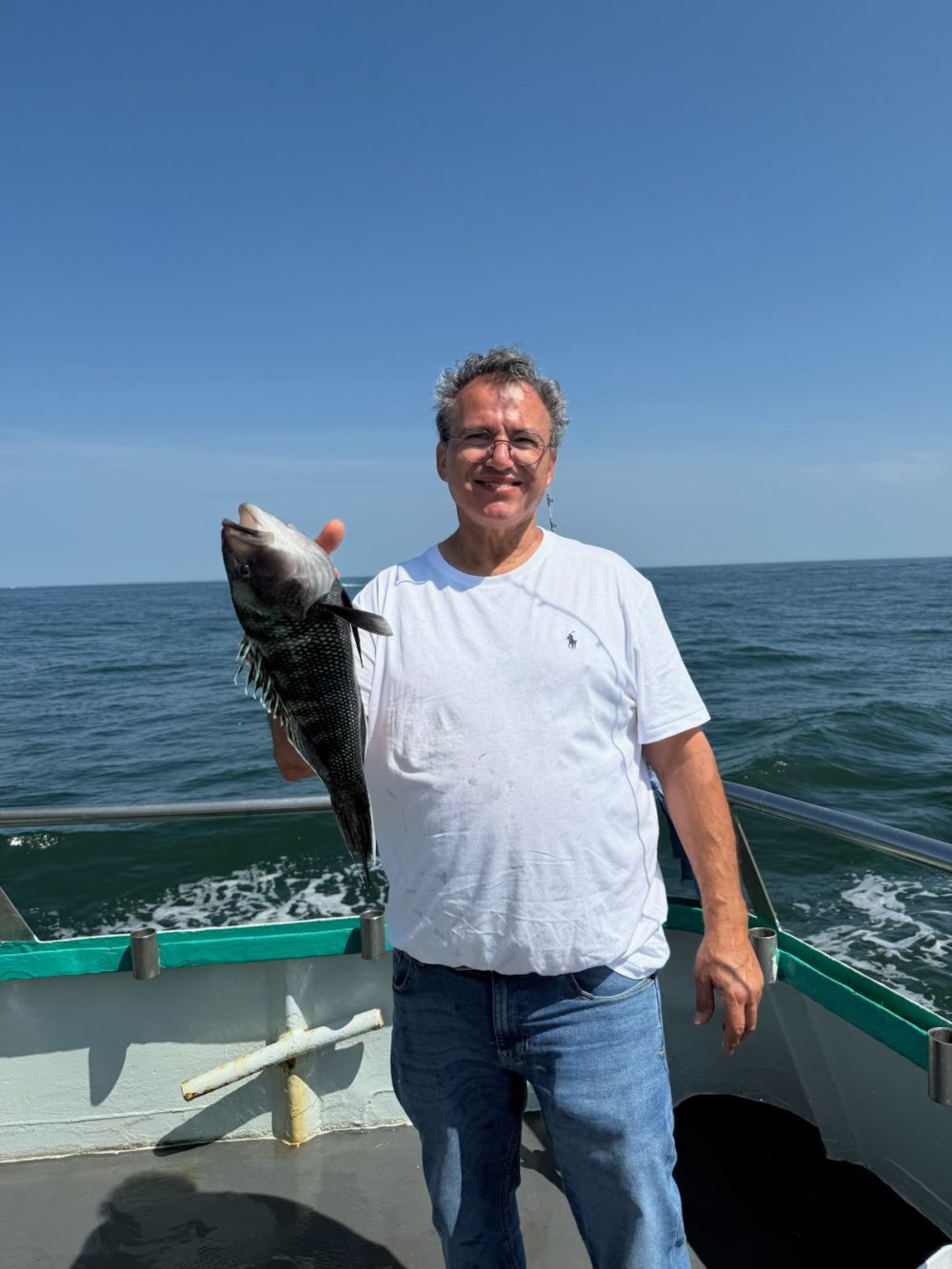 Man on a boat holding a fish with the ocean and blue sky in the background.