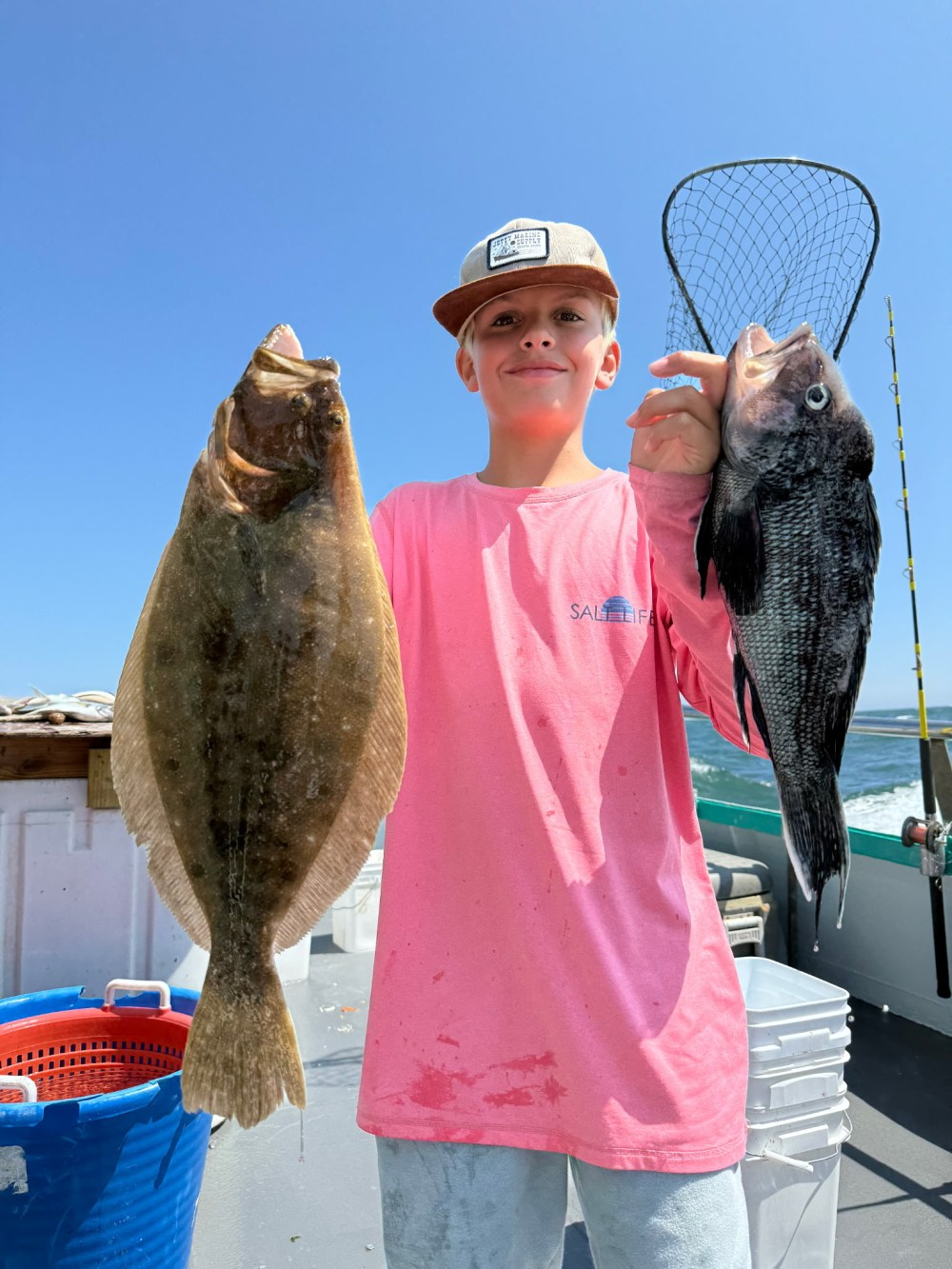 Person in pink shirt holding two fish on a boat under a clear blue sky.