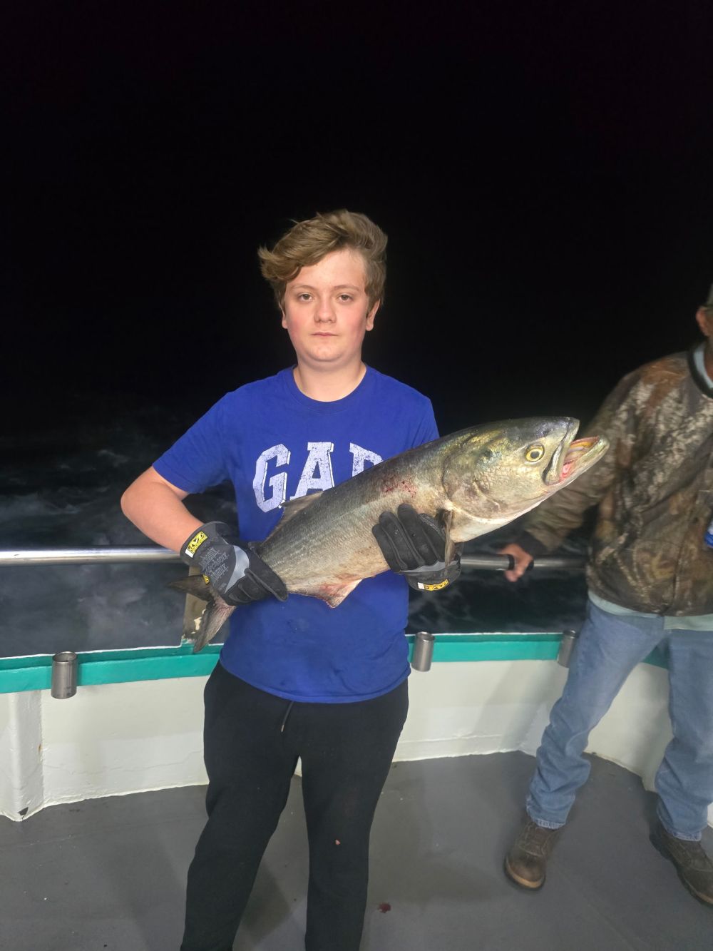 Person holding a large fish aboard a boat at night.