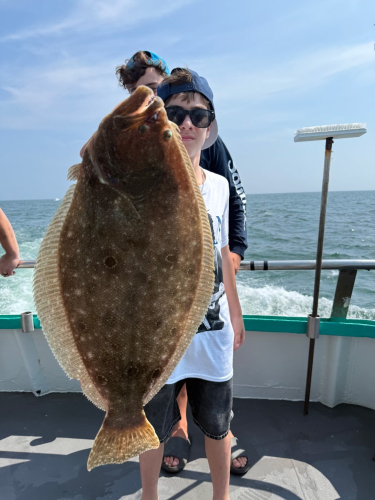 Person holding a large flatfish on a boat with the ocean in the background.