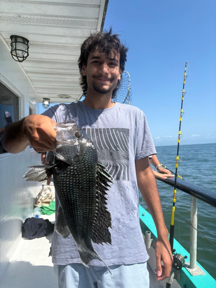 Person holding a fish on a boat with fishing rods in the background.