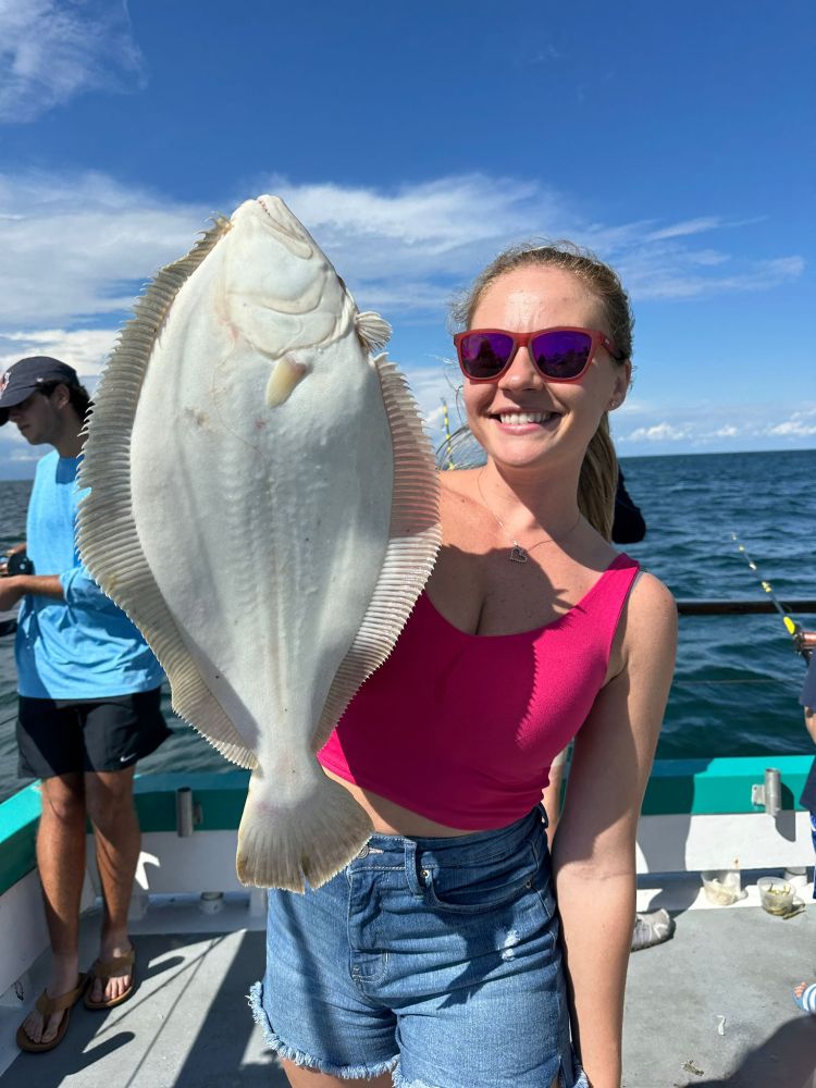 Woman in sunglasses holding a large flat fish on a boat with ocean background.