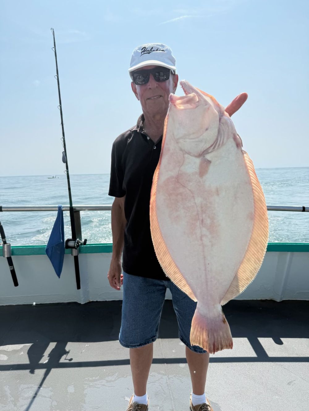 Man on a boat holding a large flat fish, wearing a cap and sunglasses.