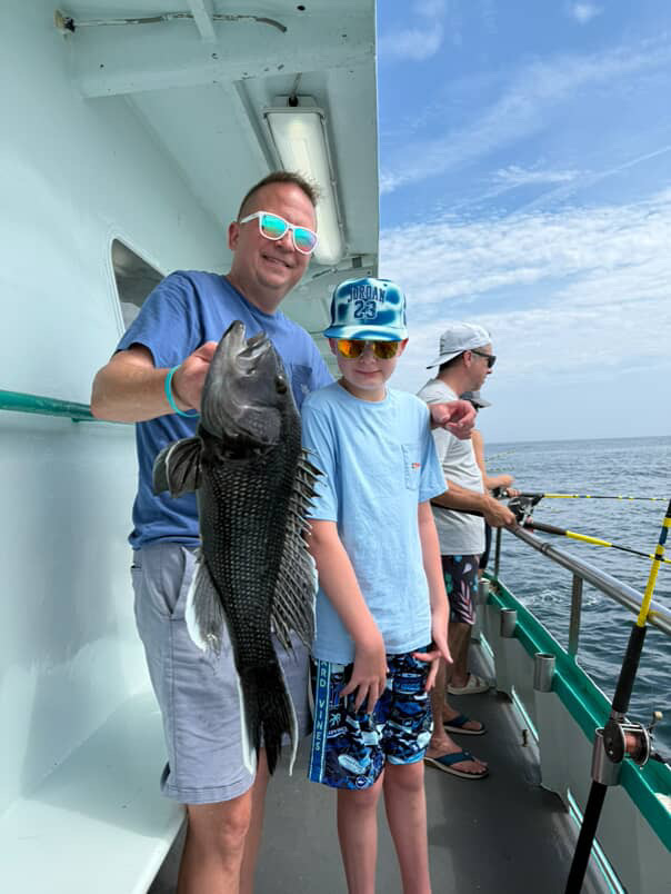 Man and boy on boat holding large fish, with two people fishing in background.