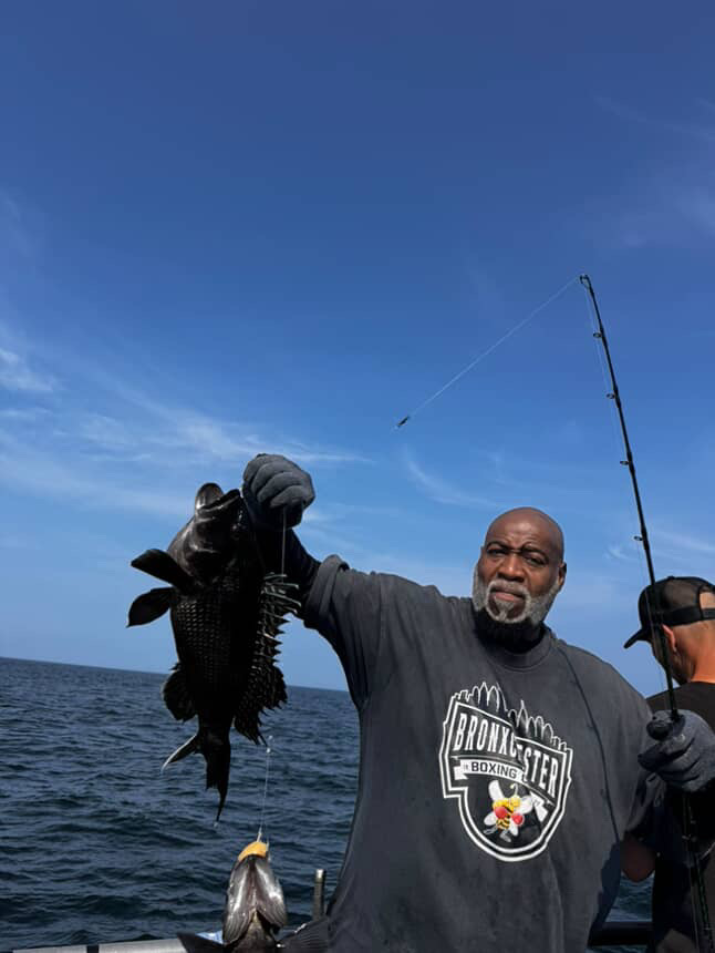 Man holding a fish on a boat with a fishing rod under a clear blue sky.