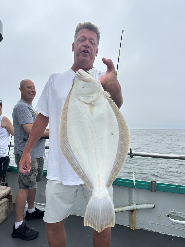 Man on boat holding a flat fish with the ocean in the background.
