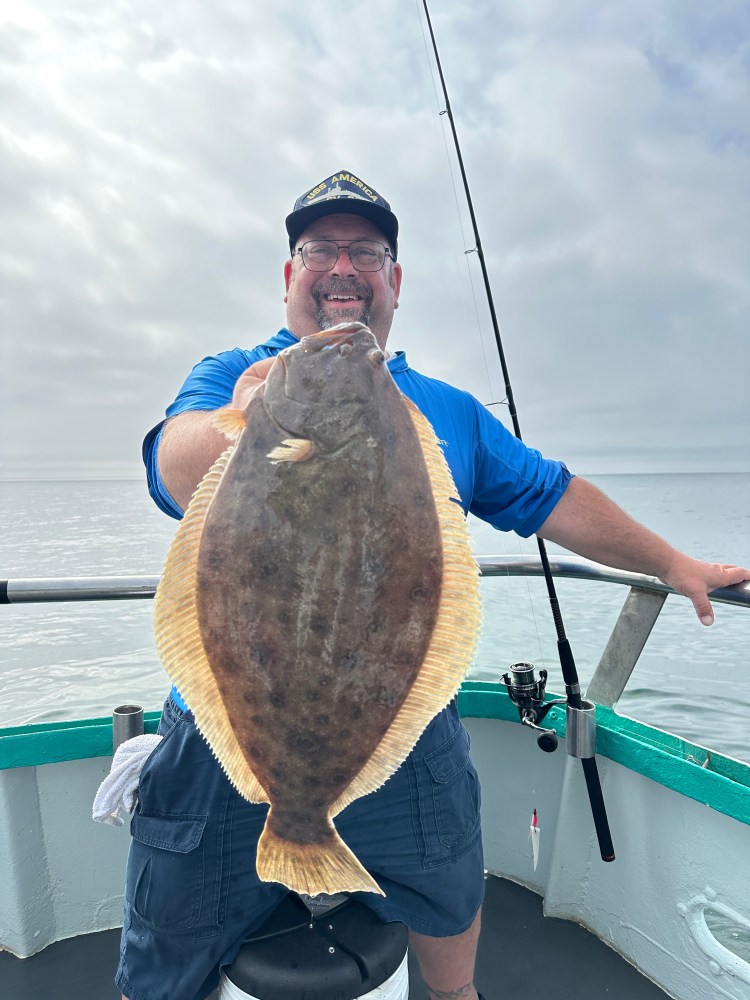Person on a boat holding a large flat fish with a fishing rod in the background.