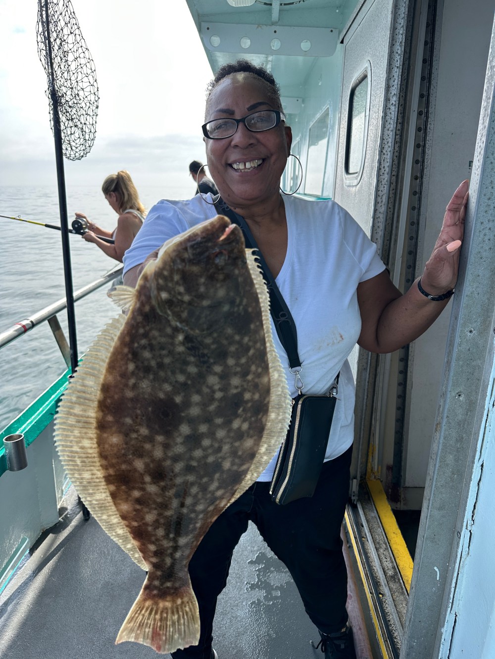 Smiling person onboard a boat holding up a large flat fish with ocean behind.