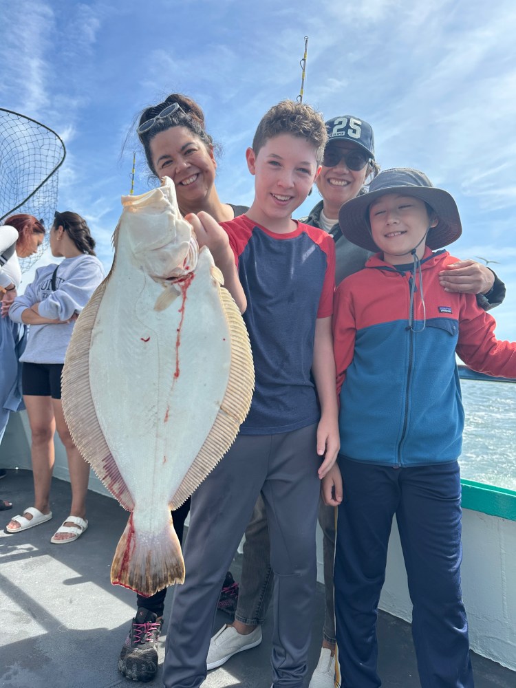 Group of people on a boat holding a large fish under a blue sky.