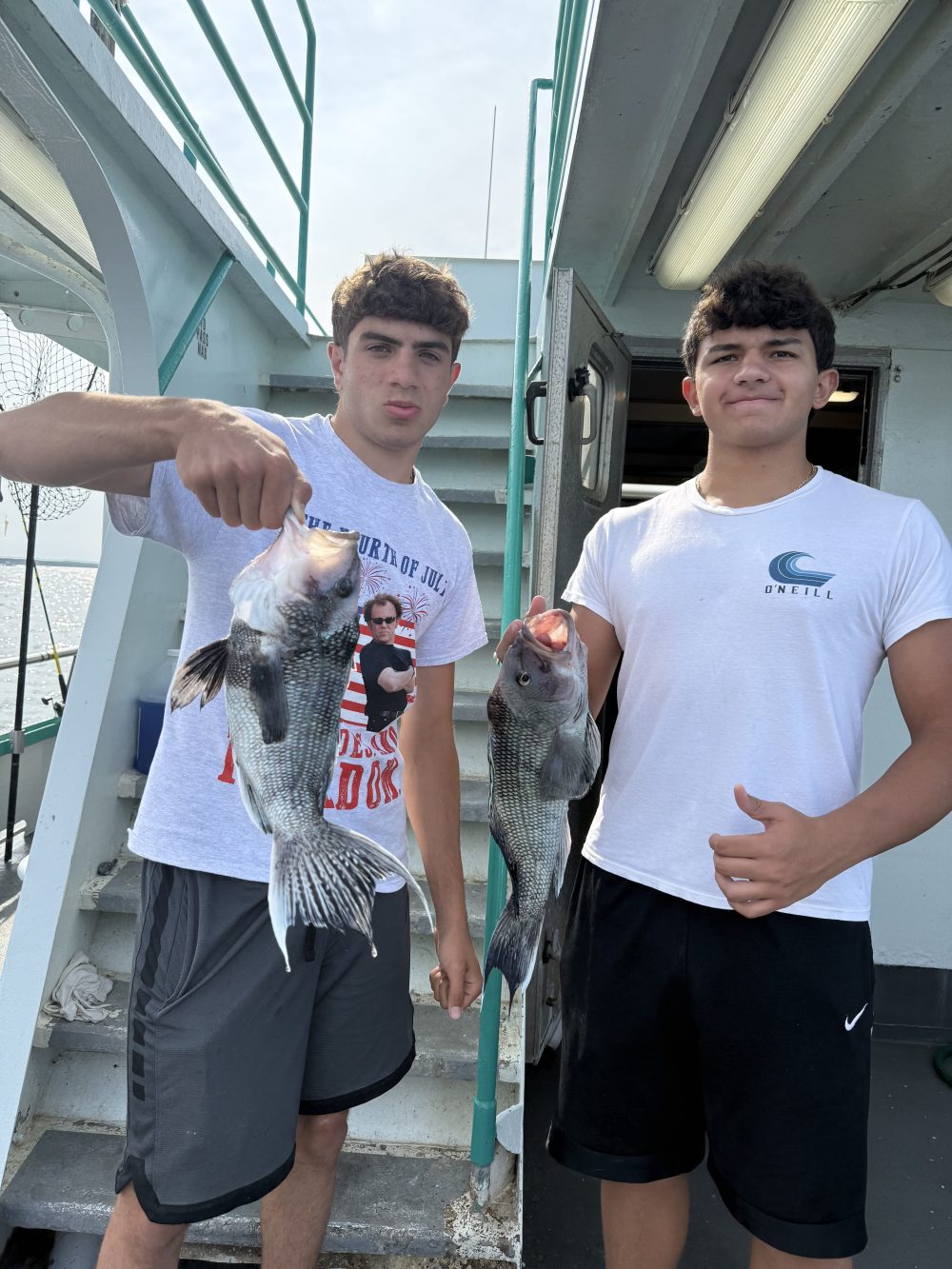 Two people on a boat holding fish, standing near a staircase.