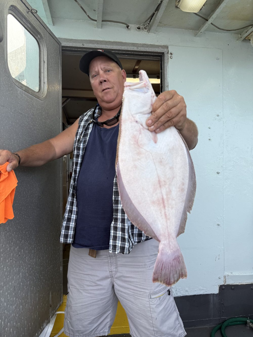 Man in cap holding a large flat fish on a boat.