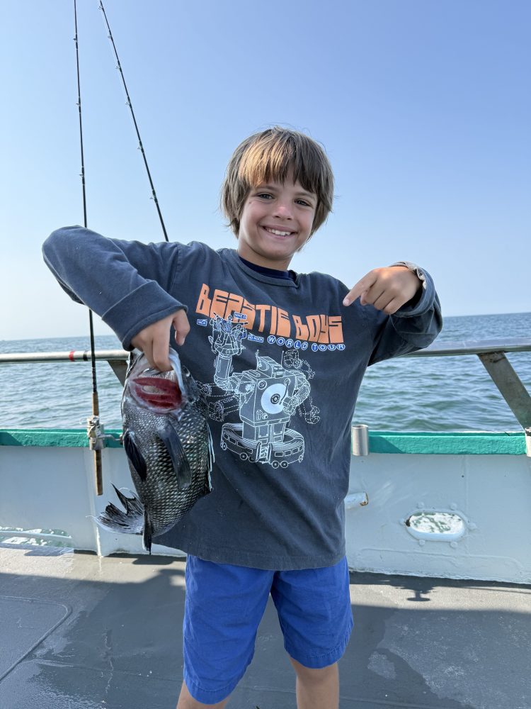 Child smiling and holding a fish on a boat with ocean in the background.
