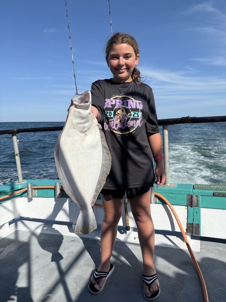 Girl on a boat holding a large fish with an ocean backdrop and clear blue sky.