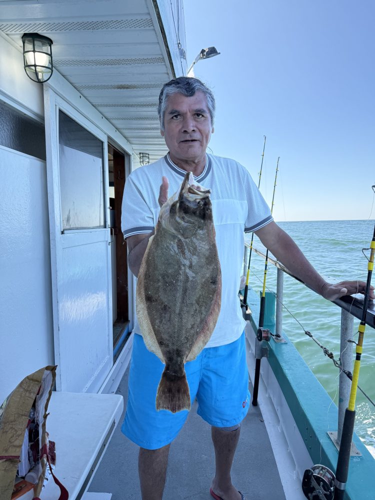 Man on boat holding a flatfish with fishing rods in the background.