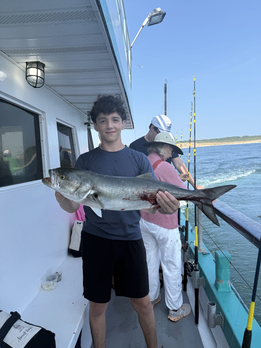 Person holding a large fish on a boat with fishing rods and ocean background.