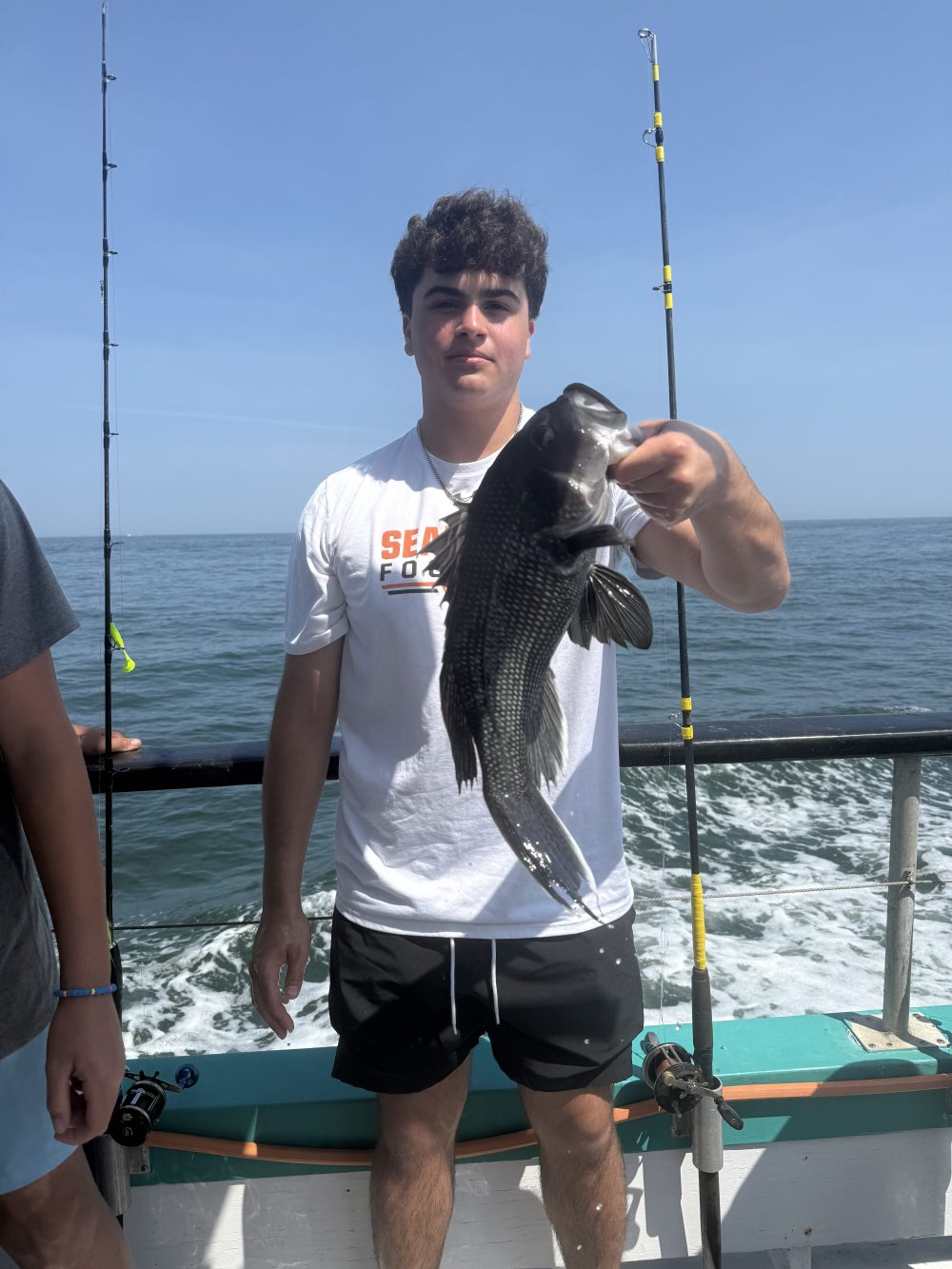 Person holding a fish on a boat with fishing rods and ocean in the background.