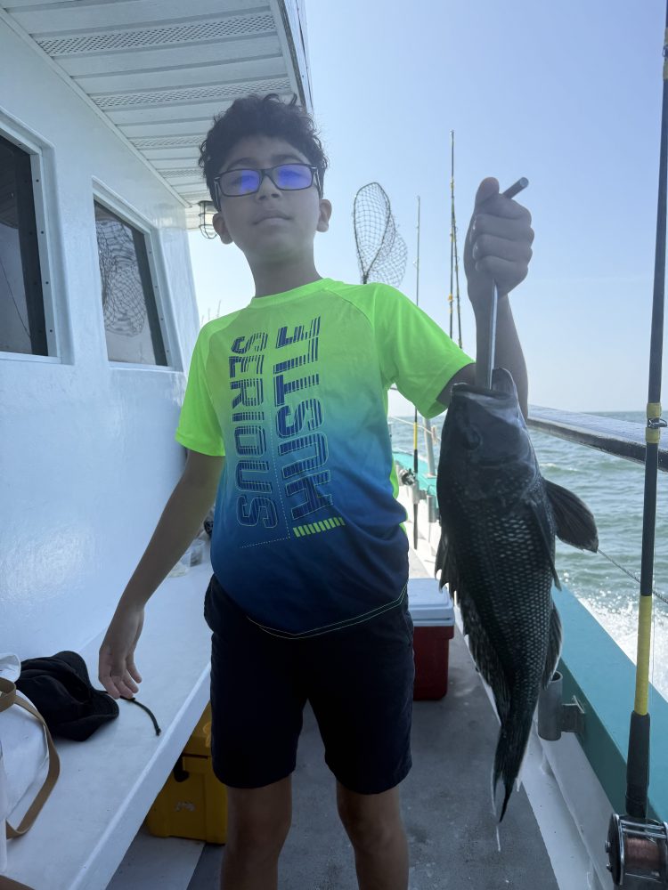 Boy on a boat holding a fish with fishing rods and blue sky in background.