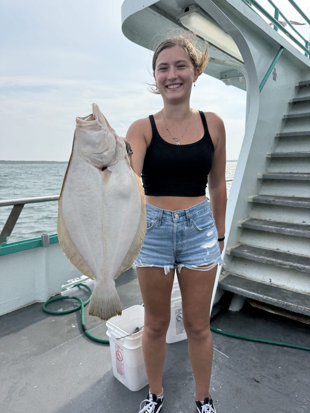 Person smiling, holding a large fish on a boat with the ocean in the background.