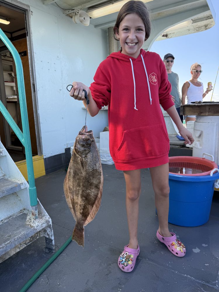 Smiling girl in red hoodie holds a fish on a boat, with two people in the background.