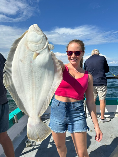 Person in red top holding a large white fish on a boat under a blue sky.