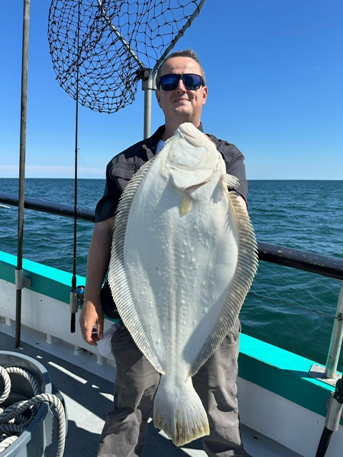 Person holding a large flat fish on a boat with ocean and blue sky background.