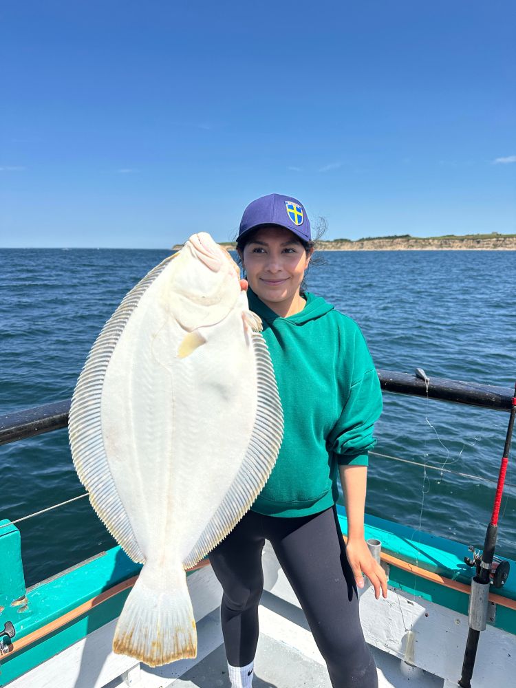 Person on a boat holding a large white fish under a clear blue sky.