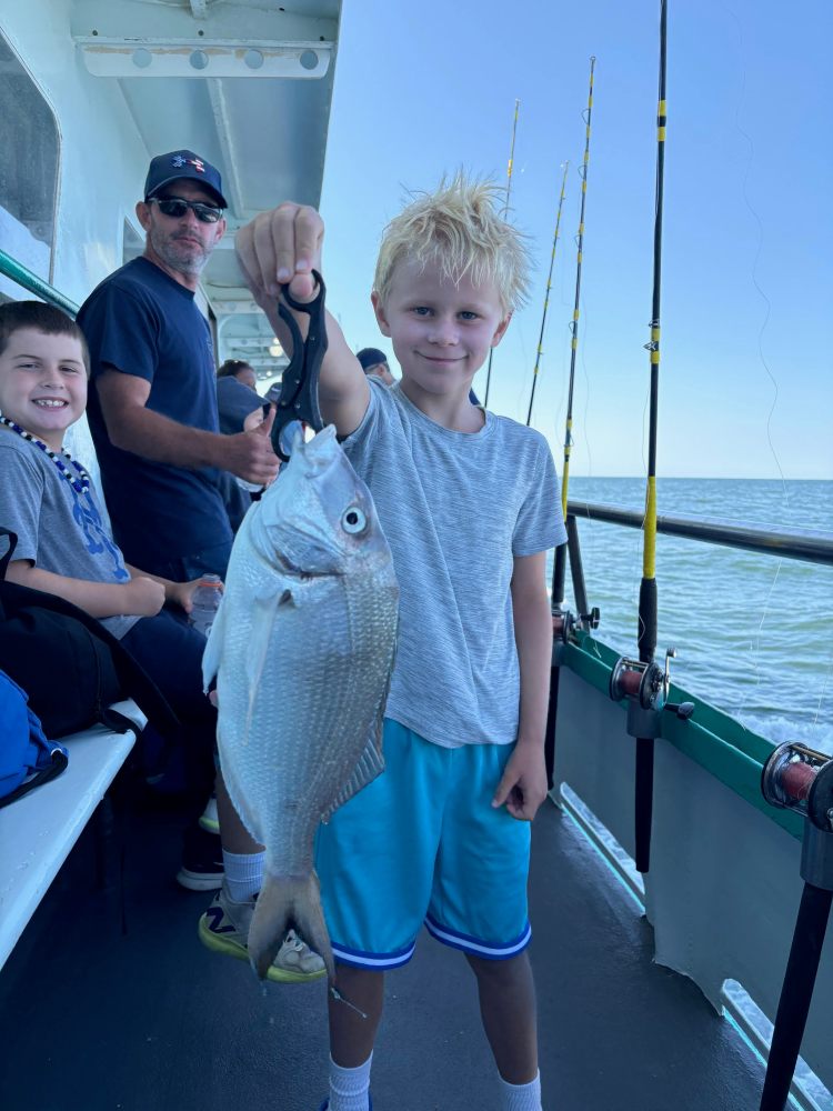Child holding a fish on a boat, with two people in the background.