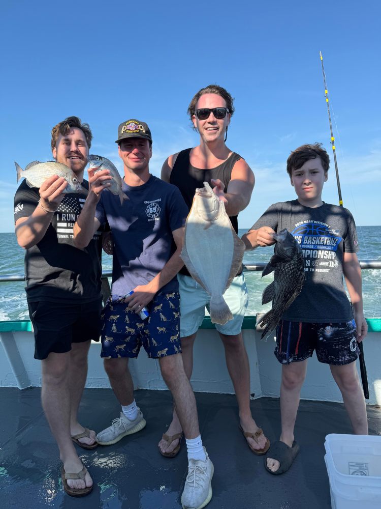 Four people on a boat holding fish with a sunny blue sky.