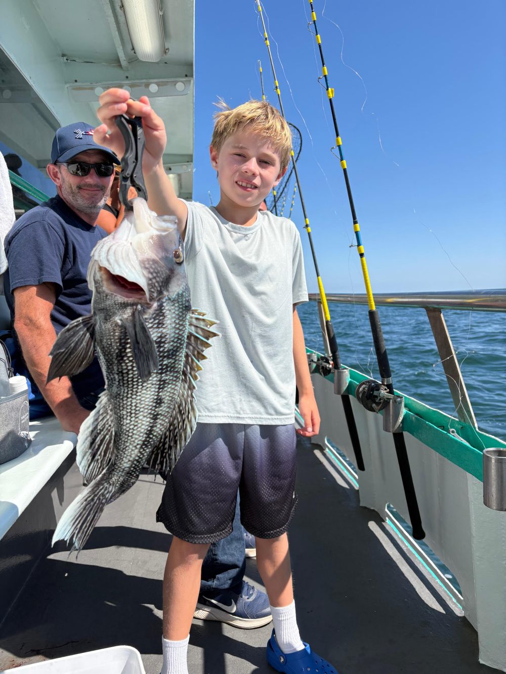 A boy on a boat holding a fish, with fishing rods in the background.