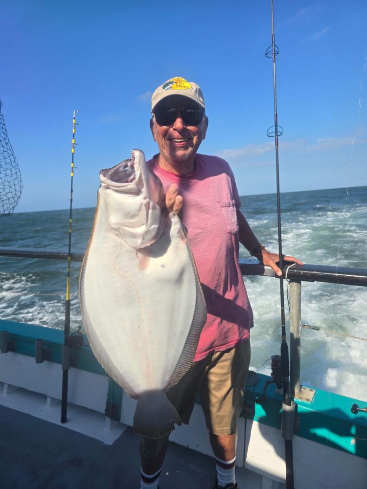 Person on a boat holding a large fish with the ocean in the background under a clear blue sky.