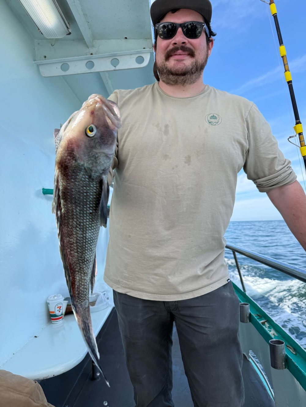 Man on boat holding a fish, wearing sunglasses and a hat.
