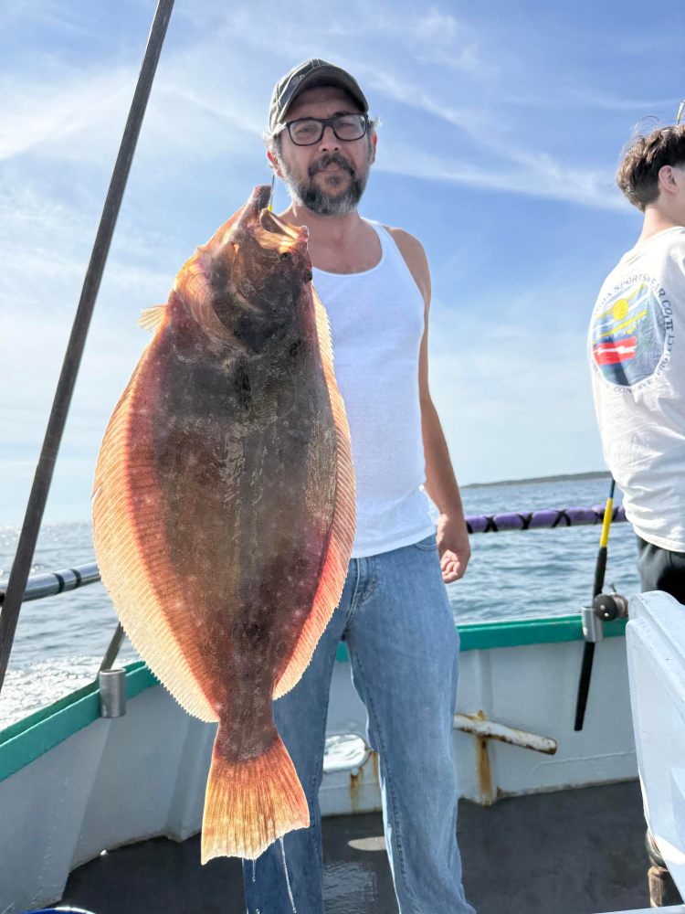Man in cap holding a large fish on a boat under a clear sky.