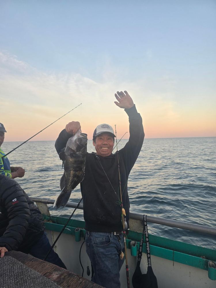 Man on boat holding a fish, smiling, with ocean and sunset in the background.