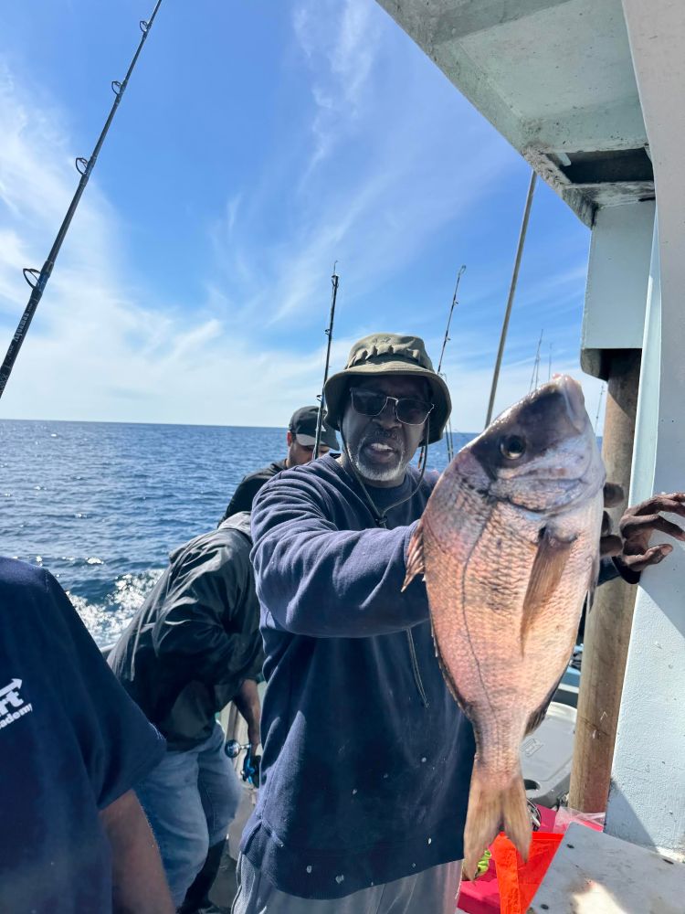 Man holding a large fish on a boat with the sea and sky in the background.
