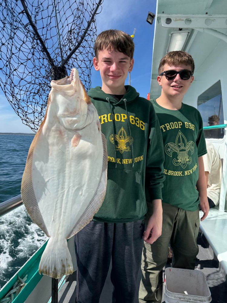 Two youths in green hoodies posing on a boat with a large flat fish in a net.