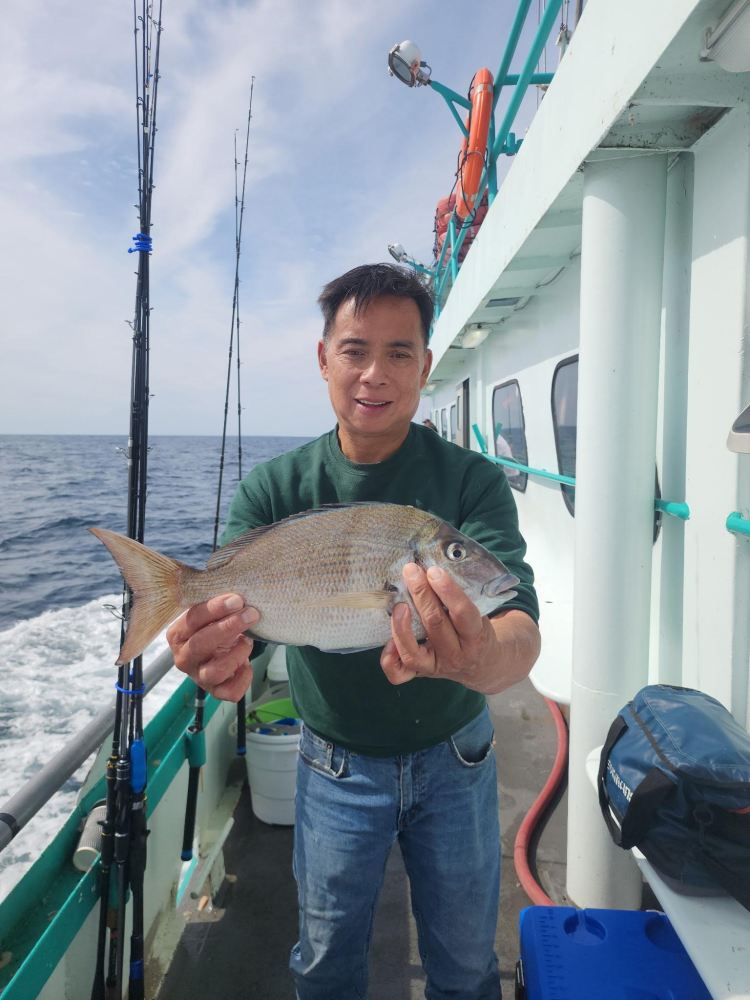 Man on a boat holding a fish with the ocean in the background.