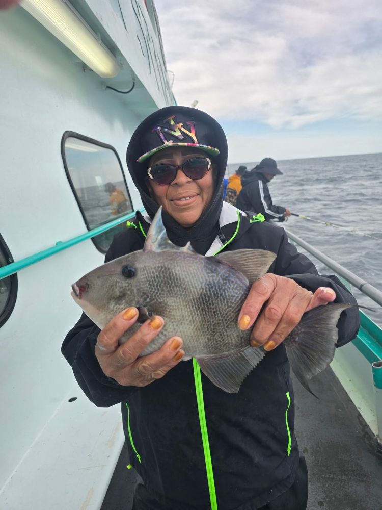 Person in sunglasses holding a fish on a boat with ocean in the background.