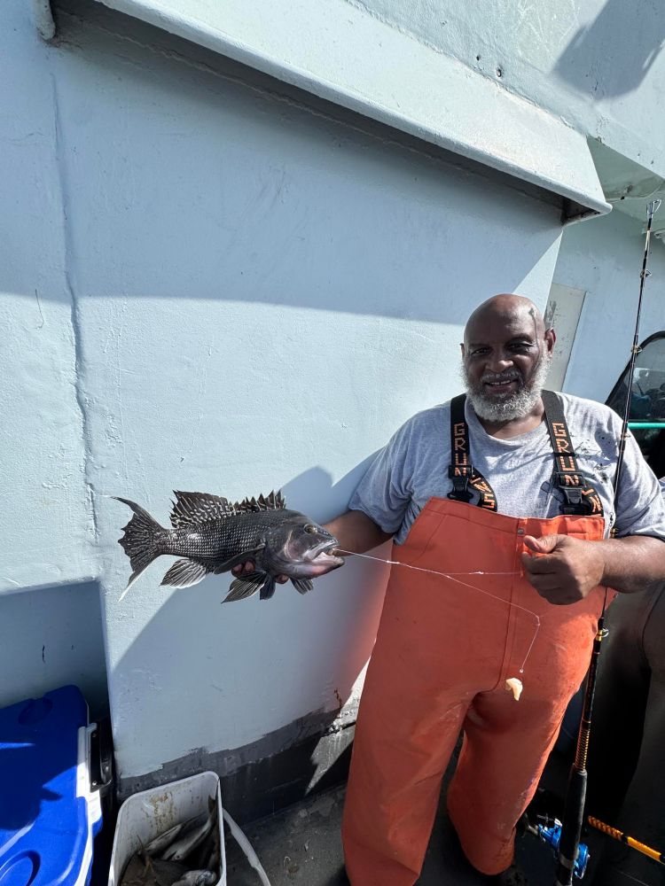 Man in orange gear holding a fish with fishing line on a boat deck.