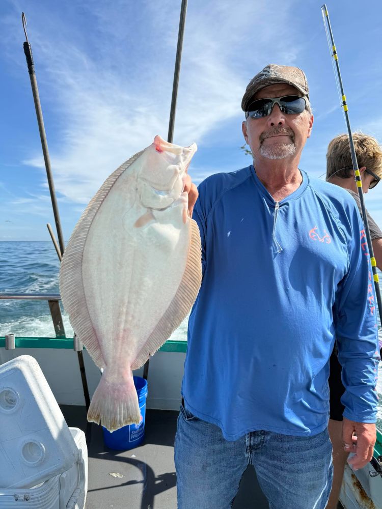 Man in blue shirt holding a large flat fish on a boat with a clear sky background.
