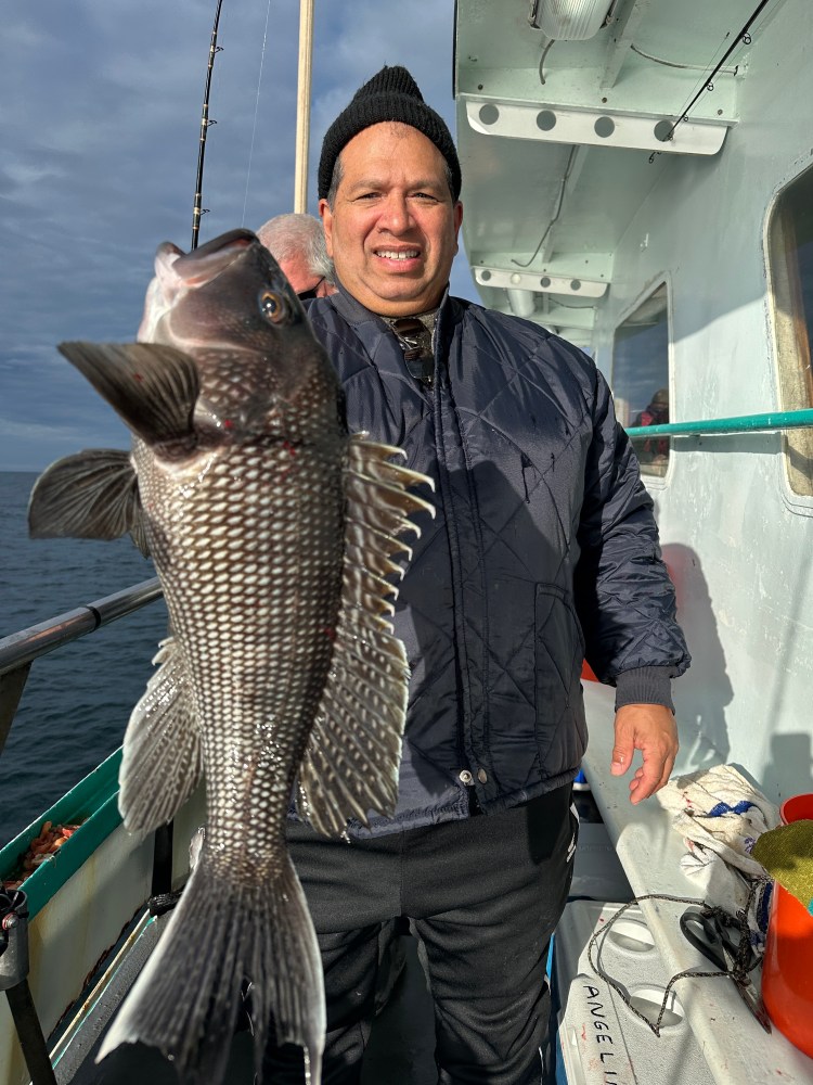Person on a boat holding a large fish towards the camera, under a cloudy sky.