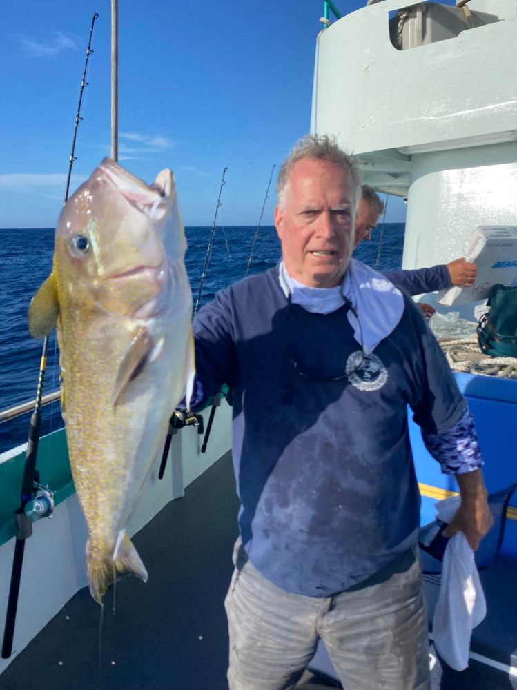 Man on boat holding a large fish with ocean in the background.