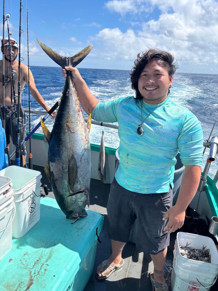 Person holding a large fish on a boat at sea, smiling under a clear sky.