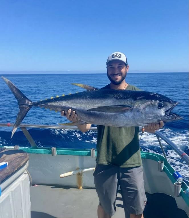 Person on a boat holding a large fish against a blue ocean backdrop.