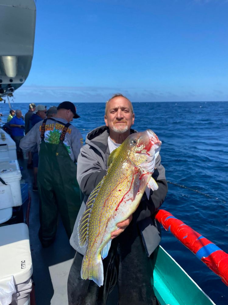 Man on boat holding a large fish, with the ocean in the background.