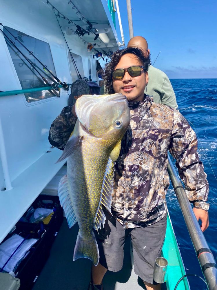 Person holding a large fish on a boat with ocean in the background.