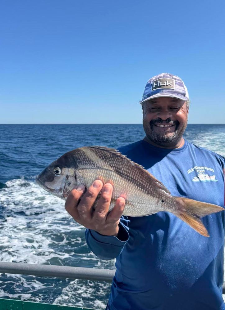 Man on a boat holding a fish with the ocean in the background.