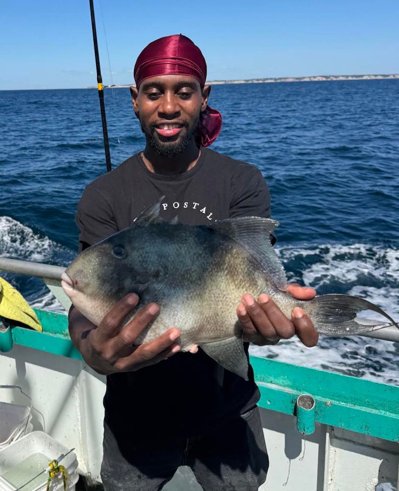 Person holding a large fish on a boat with the ocean in the background.